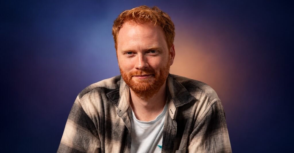 Orbit Acquires Four New Richard Swan Fantasy Novels Richard Swan in a checked shirt against a blue, violet and warm copper gradient background.